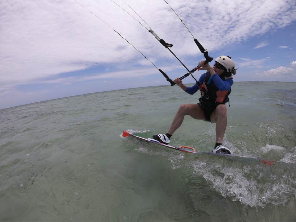 Kippy kiteboarding across the water beneath a cloudy blue sky.