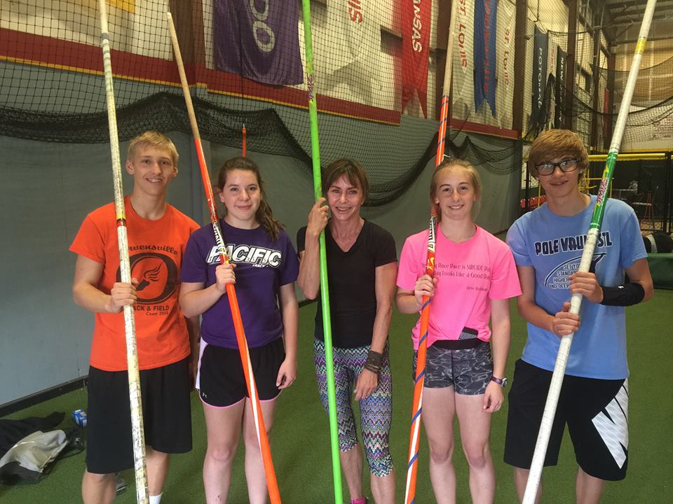 Kippy Hoene smiling with four younger pole-vaulting students, each holding a vaulting pole.
